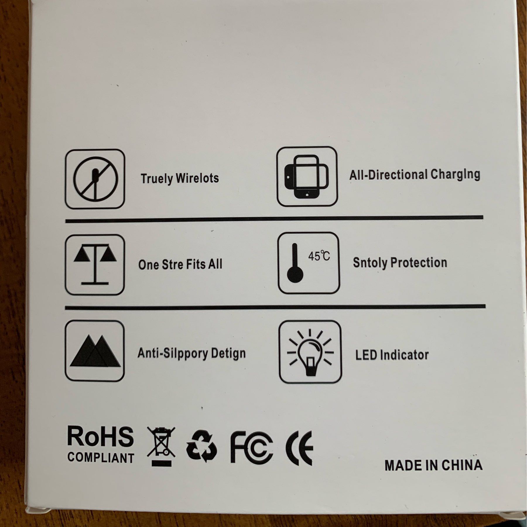The back of a budget wireless charger box for my iPhone. with features like "Truely Wirelots" "One Stre Fits All" and "Sntoly Protection".