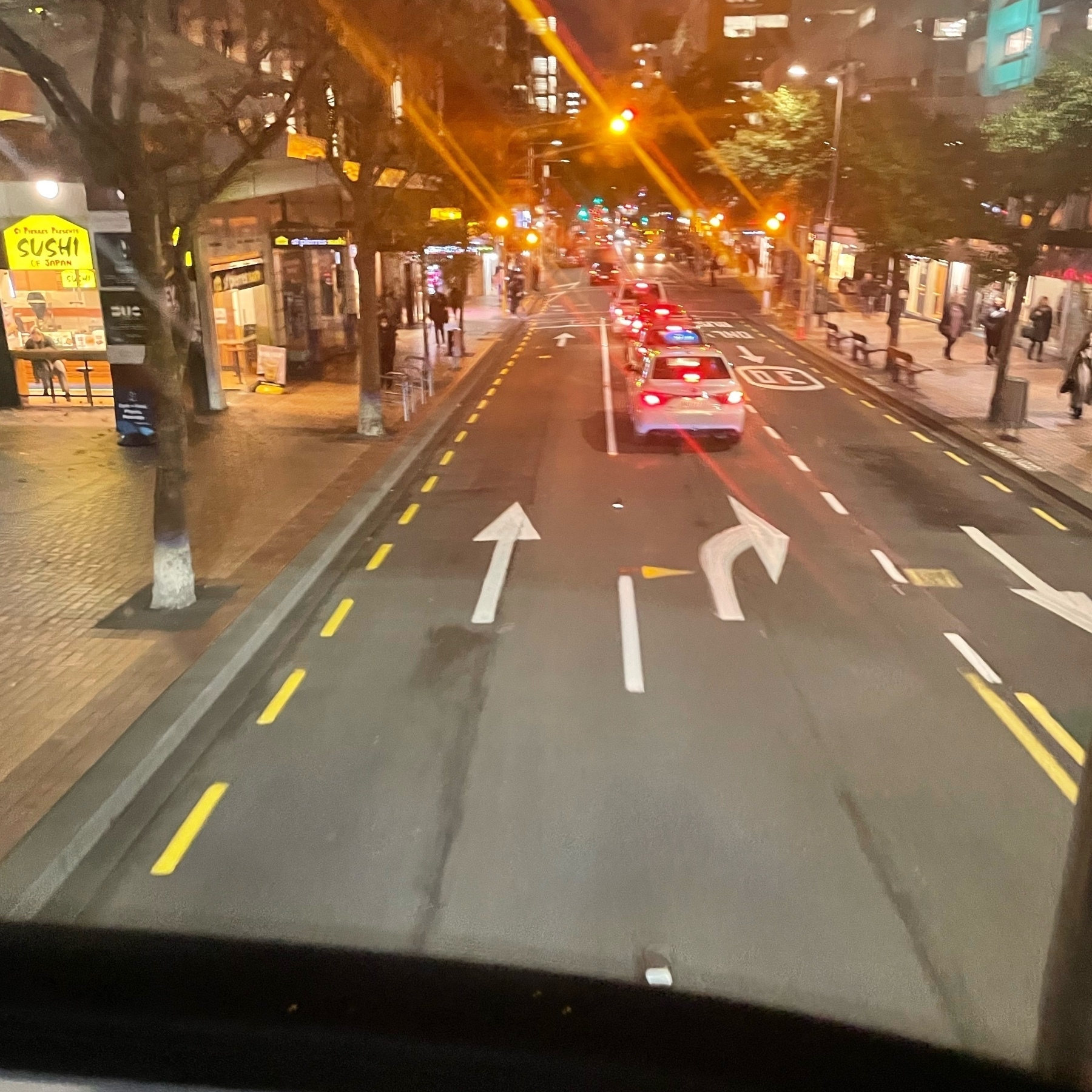 A photo taken from the top deck of a electric double decker bus while travwlling theough Pōneke/Wellington city. It is dark and the traffic and rear lights of cars below are creating a light show through the lens flare. 